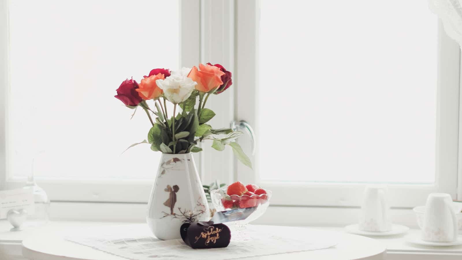 Blomster i vase og jordbær på bord ved vindu på Gamlebyen Hotell i Fredrikstad.