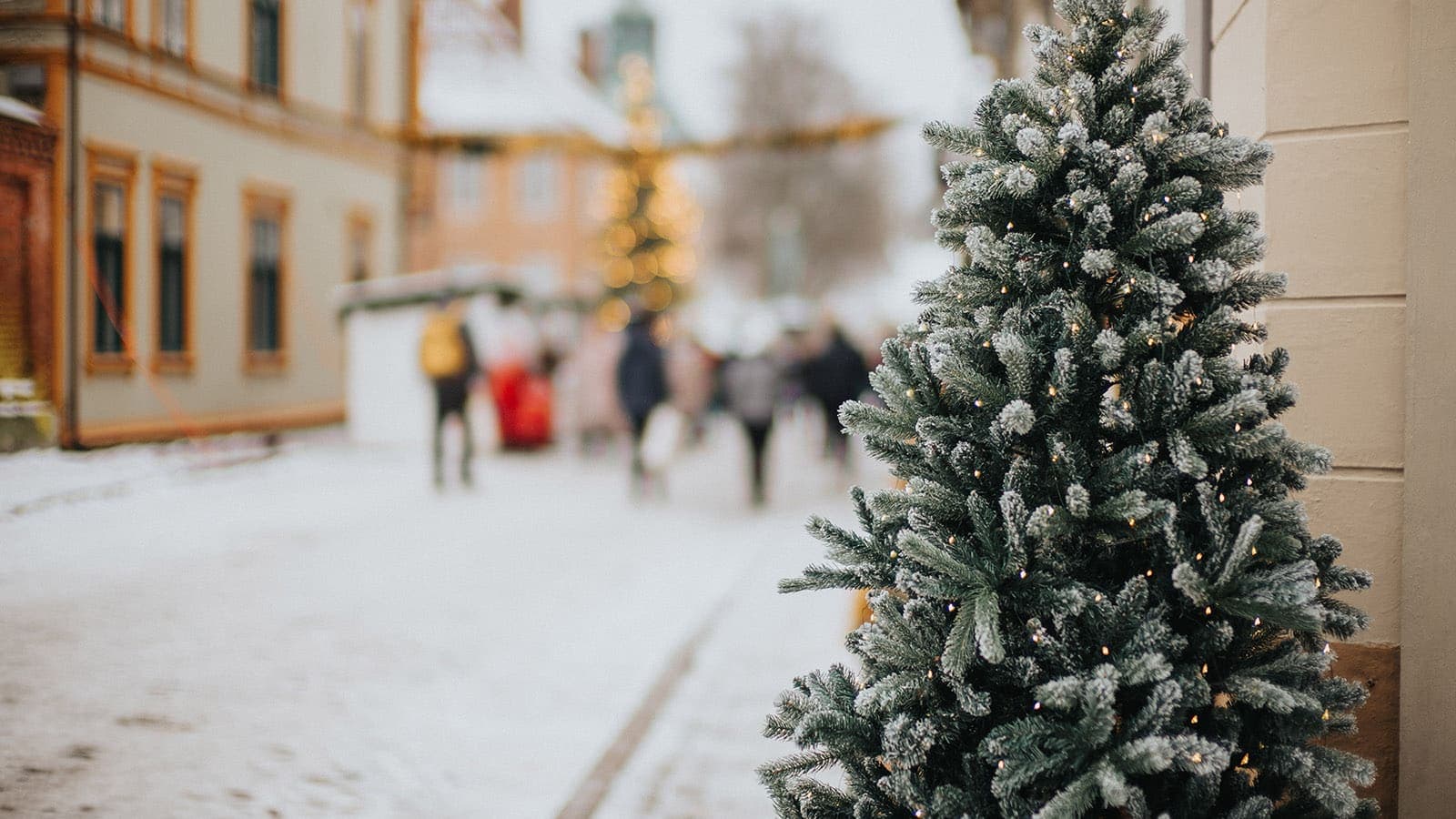 Snødekket gate med pyntet juletre og mennesker i bakgrunnen.