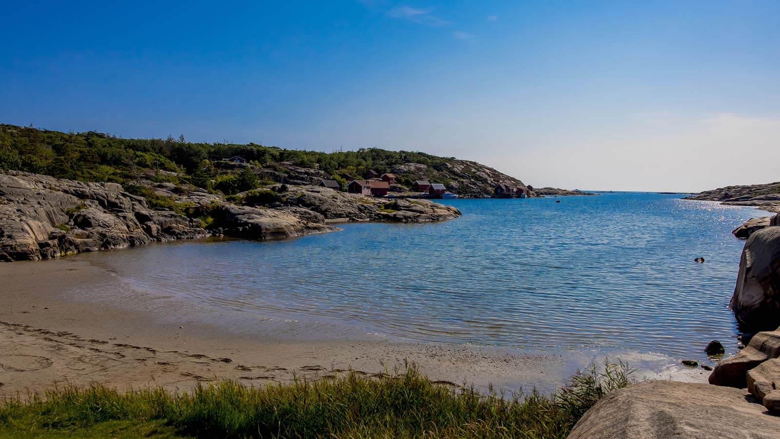 Kuvauen sett fra svaberg, med klart vann og røde sjøboder i det fjerne.