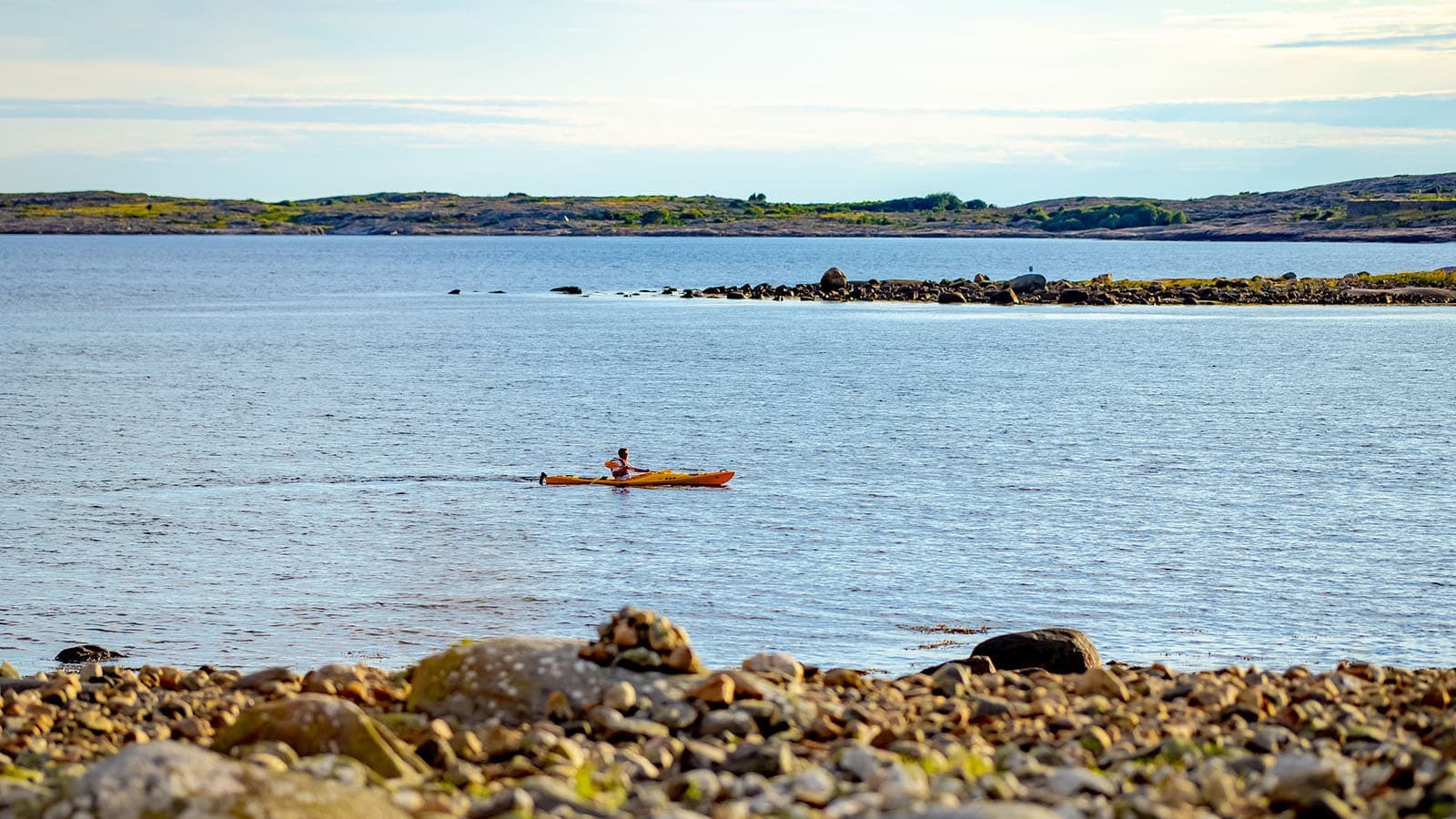 Kajakkpadler på stille sjø, sett fra svabergene ved Brattestø på Asmaløy, med Akerøya i bakgrunnen.