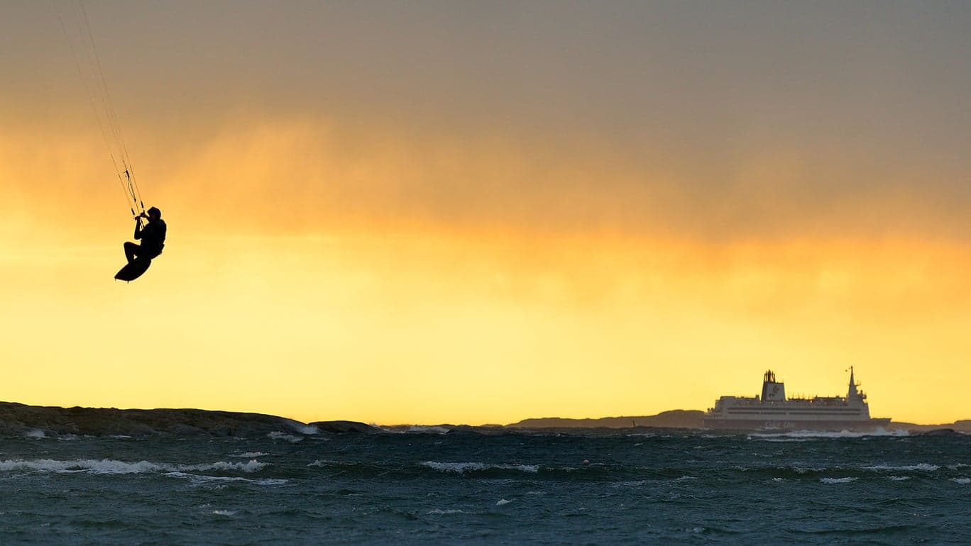 Kiter i lufta over havet i Ørekroken, med ferge i horisonten ved solnedgang.