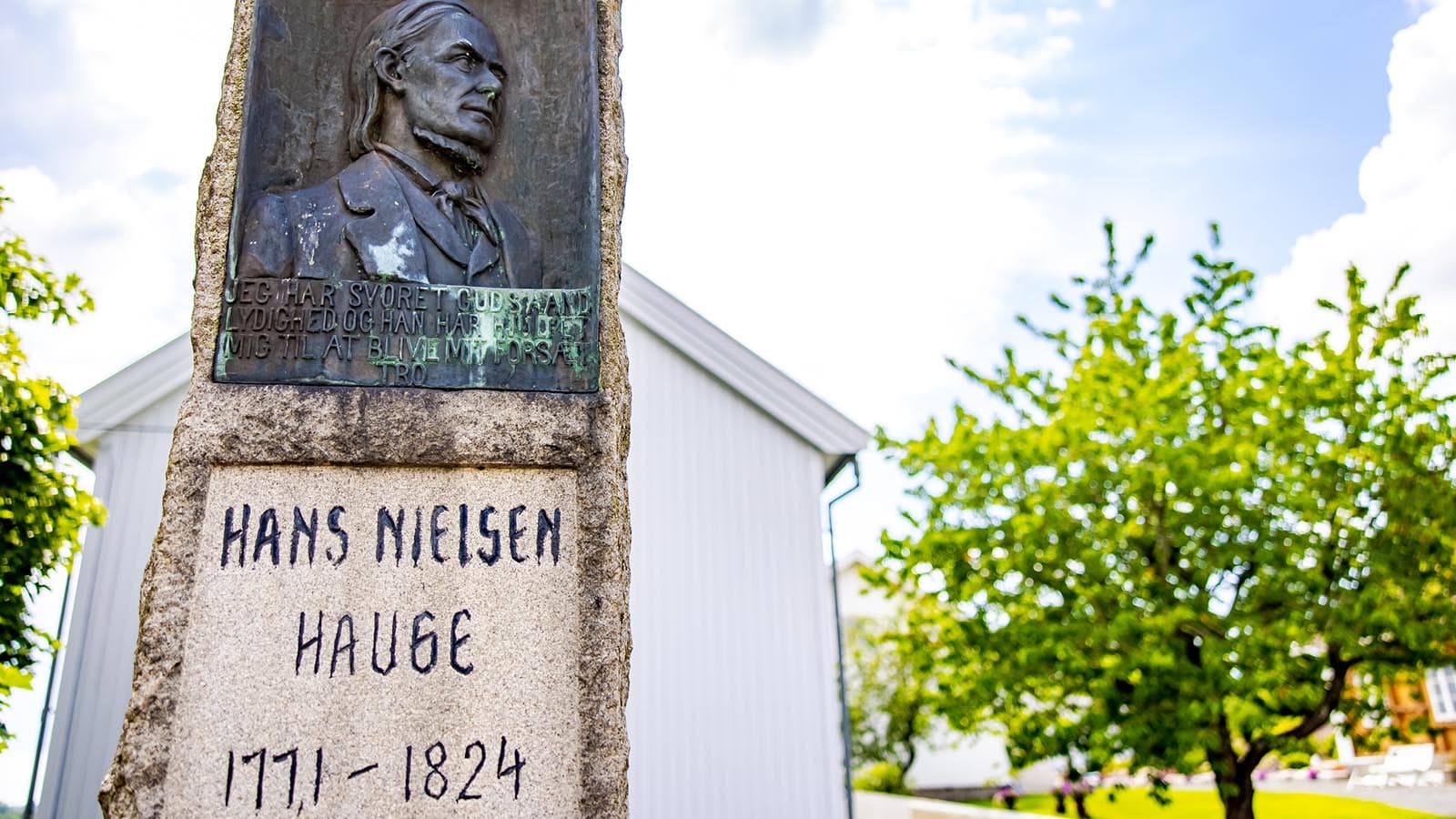 Minnestein med relieff av Hans Nielsen Hauge og inskripsjon foran barndomshjemmet på Rolvsøy.