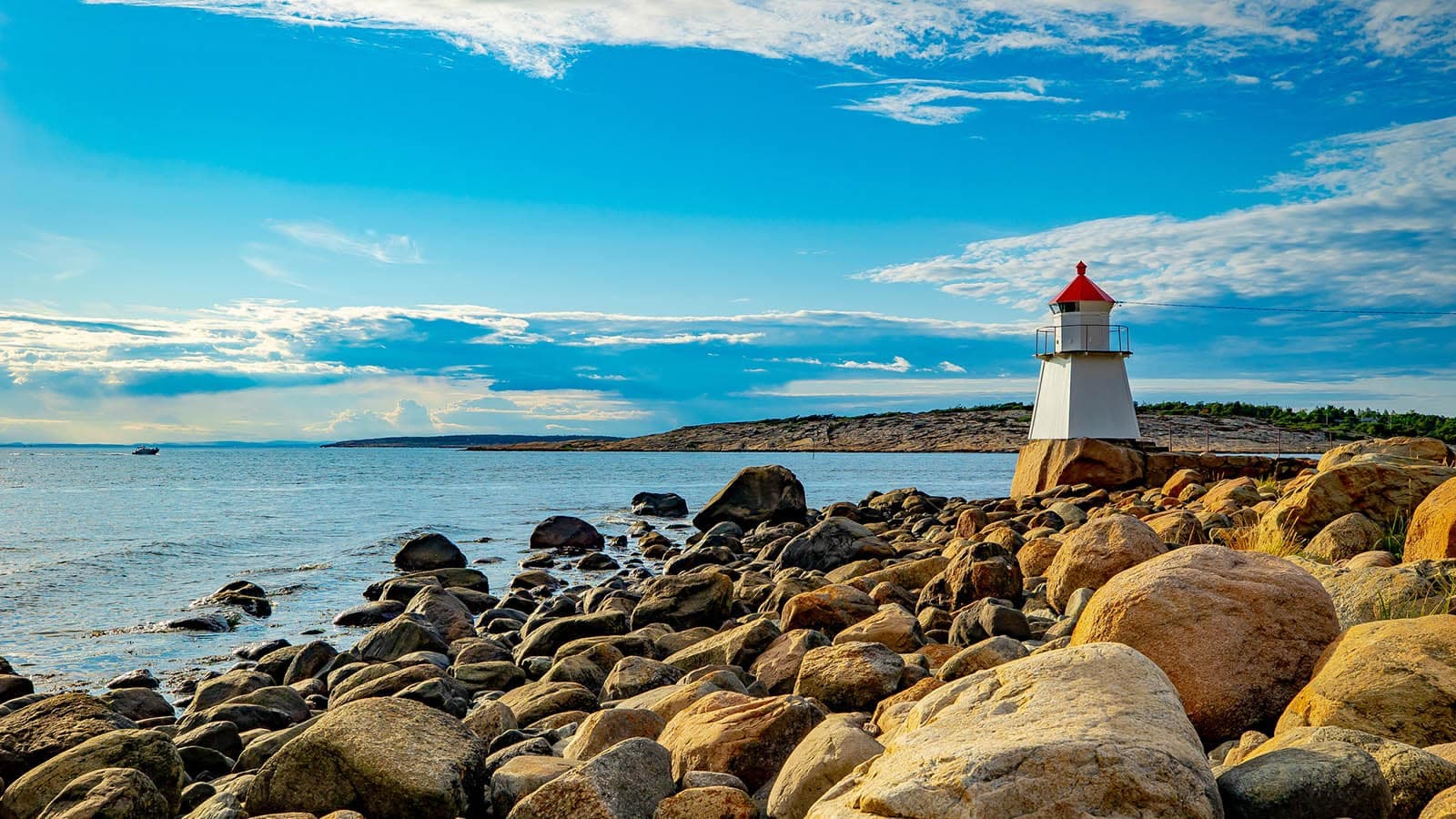 Pikesten fyr på Asmaløy i Hvaler, omgitt av svaberg og steiner med utsikt over havet under blå himmel.