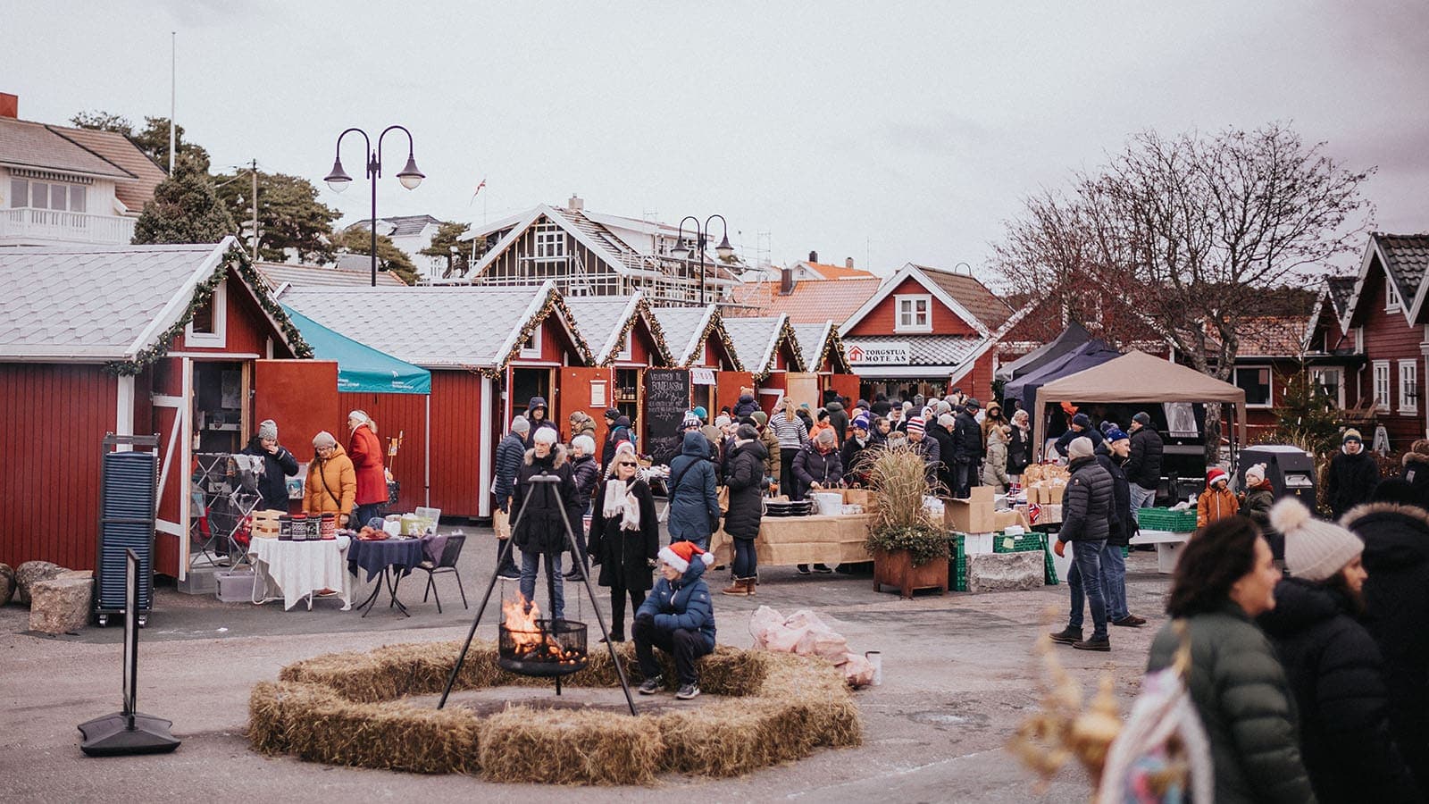 Folk går mellom bodene og handler på julemarkedet, mens julestemningen skapes av lys, pynt og lukt av mat.